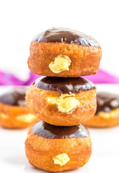 Stack of three Boston Cream Donuts on top of each other, more donuts in background.