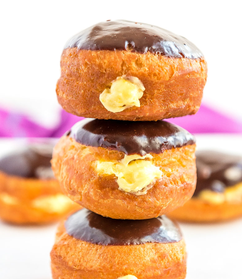 Stack of three Boston Cream Donuts on top of each other, more donuts in background.