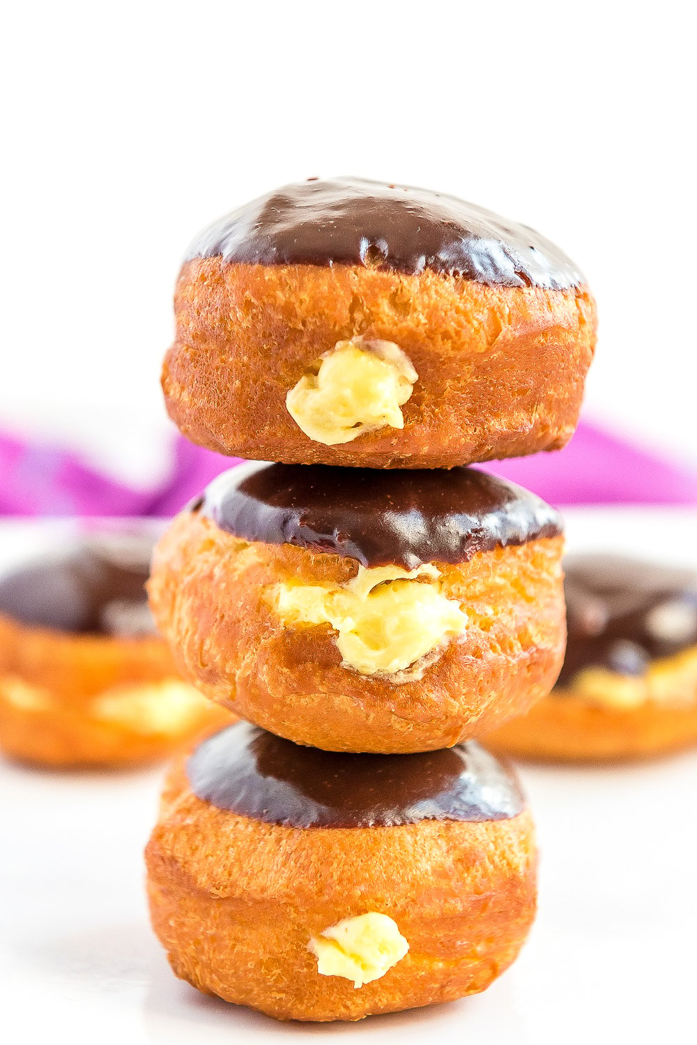 Stack of three Boston Cream Donuts on top of each other, more donuts in background.