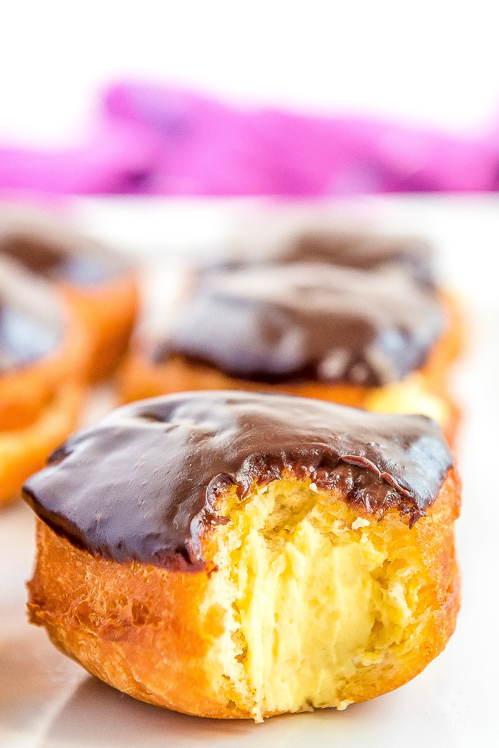 Boston Cream Donut on white plate with a bite taken out of it showing the filling inside.