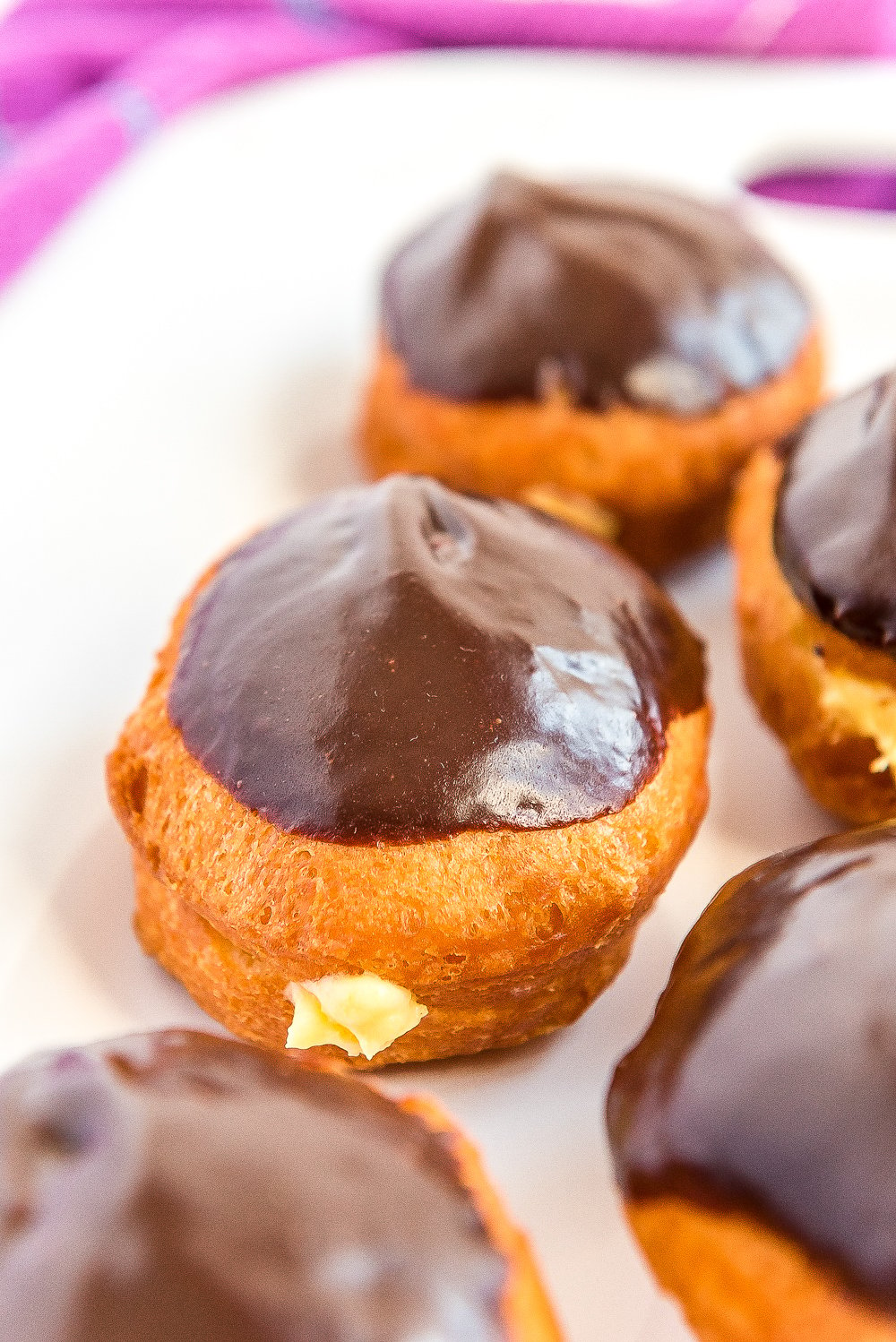 Boston Cream Donuts on a white plate with a purple napkin.