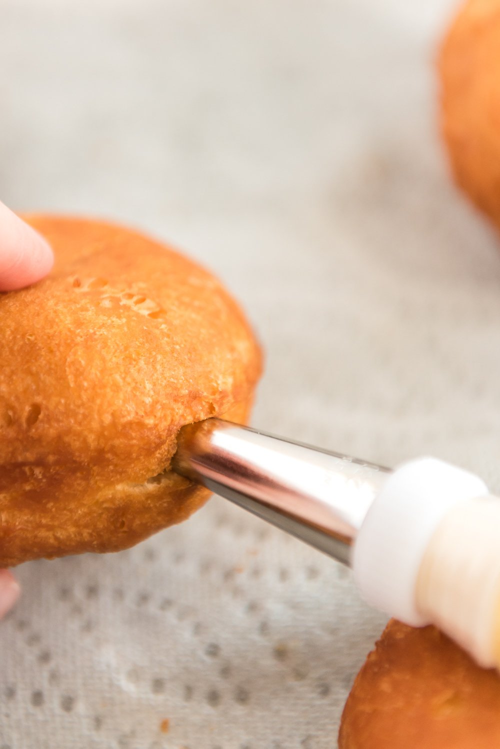 Vanilla pastry filling being piped into a cooked donut.