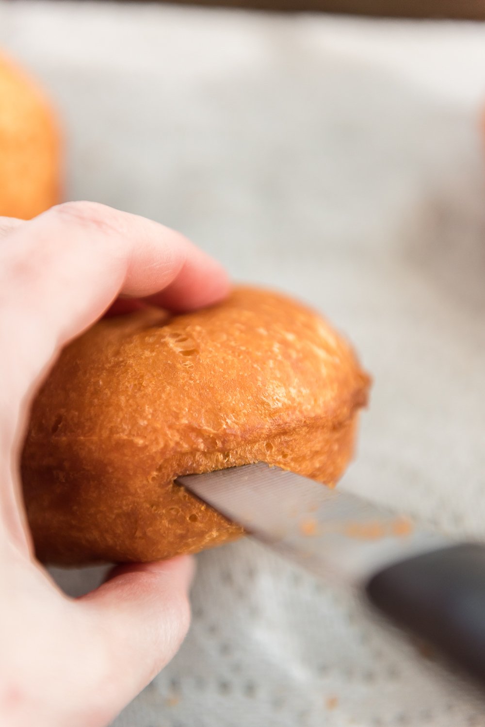 Paring knife being used to cut a slit in the side of a donut to add filling.