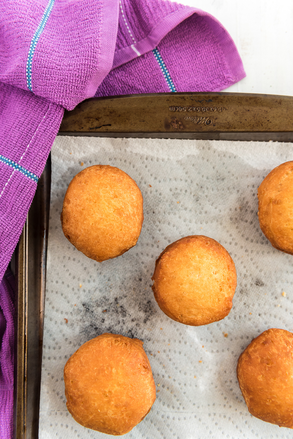 Fried donuts on a paper towel-lined baking sheet with purple napkin.