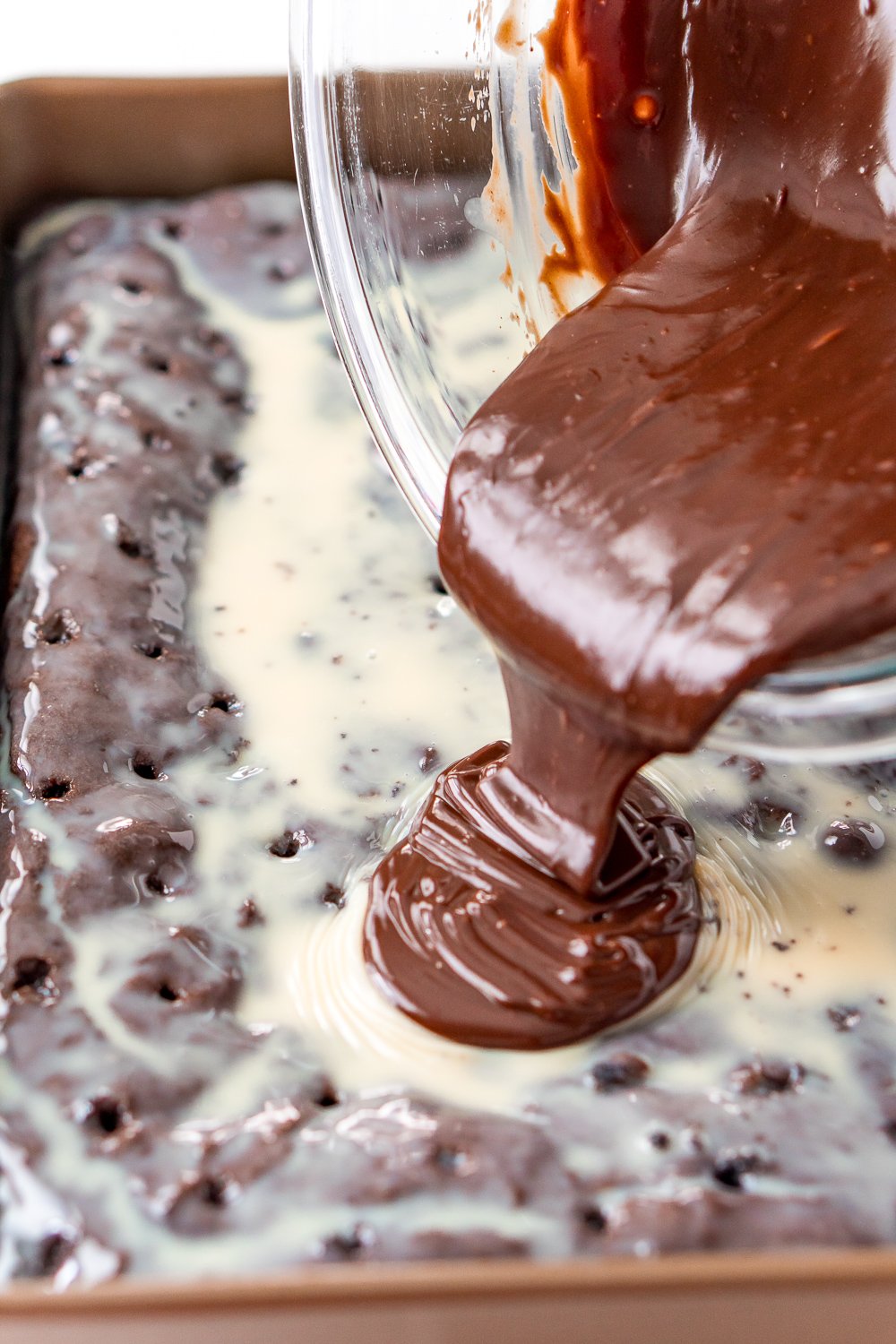 Chocolate ganache being poured over the top of a chocolate cake.