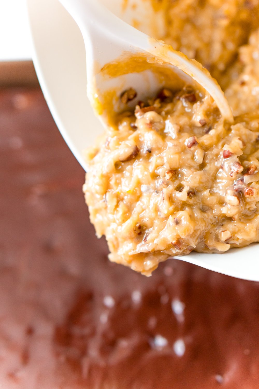 Coconut Pecan Frosting being poured onto a chocolate cake.