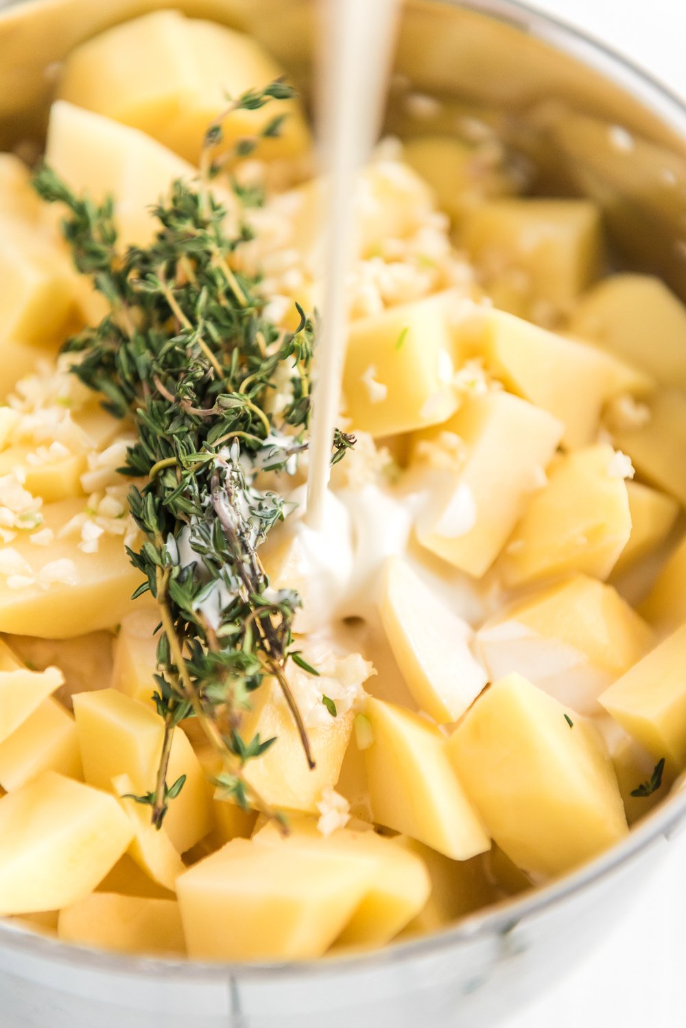 Milk being poured into pot with chopped potatoes, thyme, and garlic.