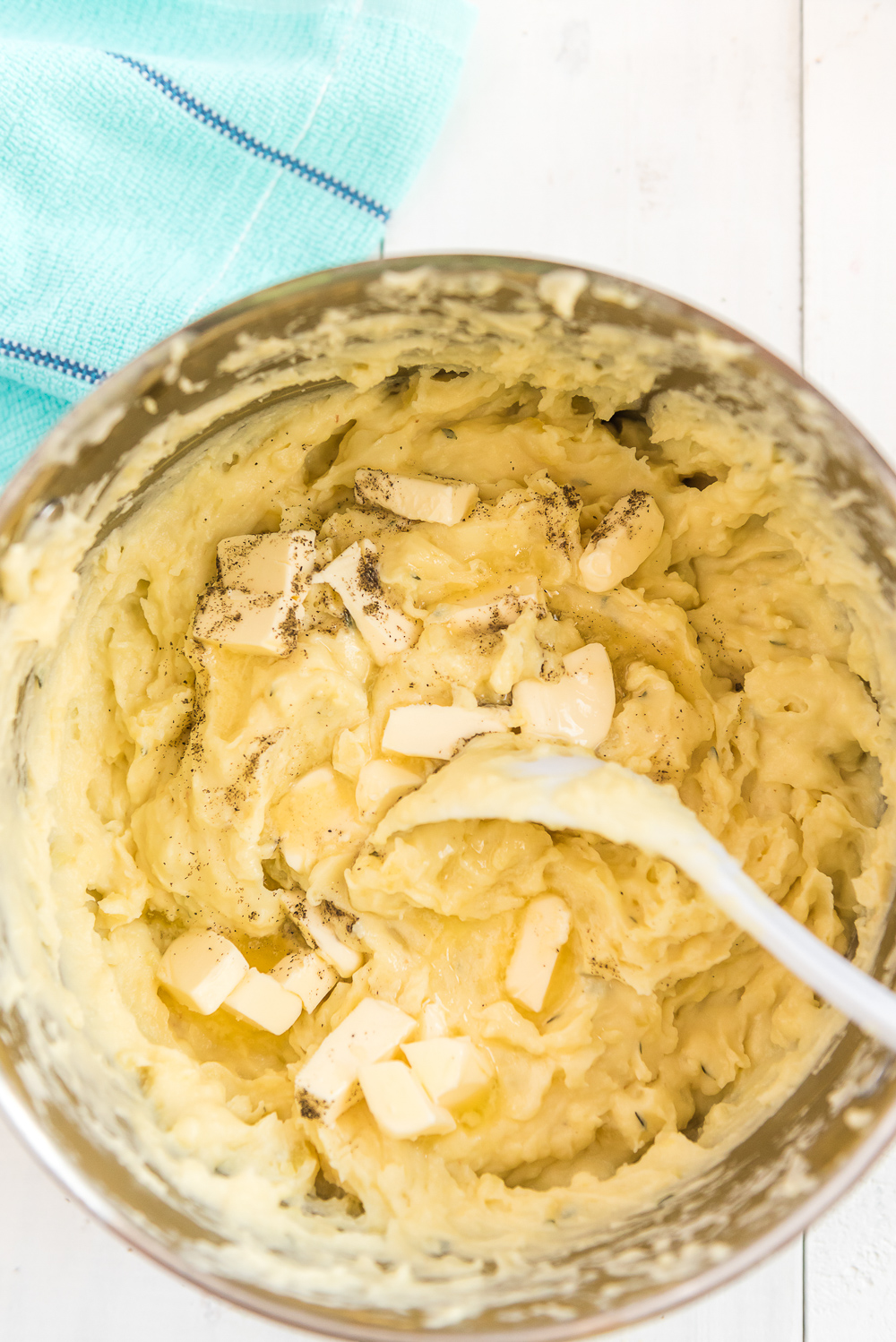 Overhead photo of butter, salt, and pepper being stirred into a pot of mashed potatoes.