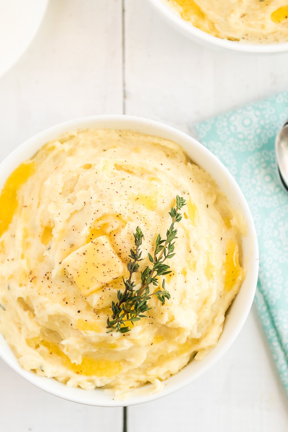 Overhead photo of Creamy Mashed Potatoes in a white bowl on white wood table with blue napkin.