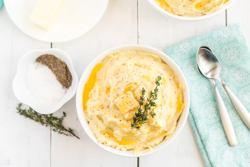 White bowl full of Creamy Garlic Mashed potatoes with salt, pepper and thyme.