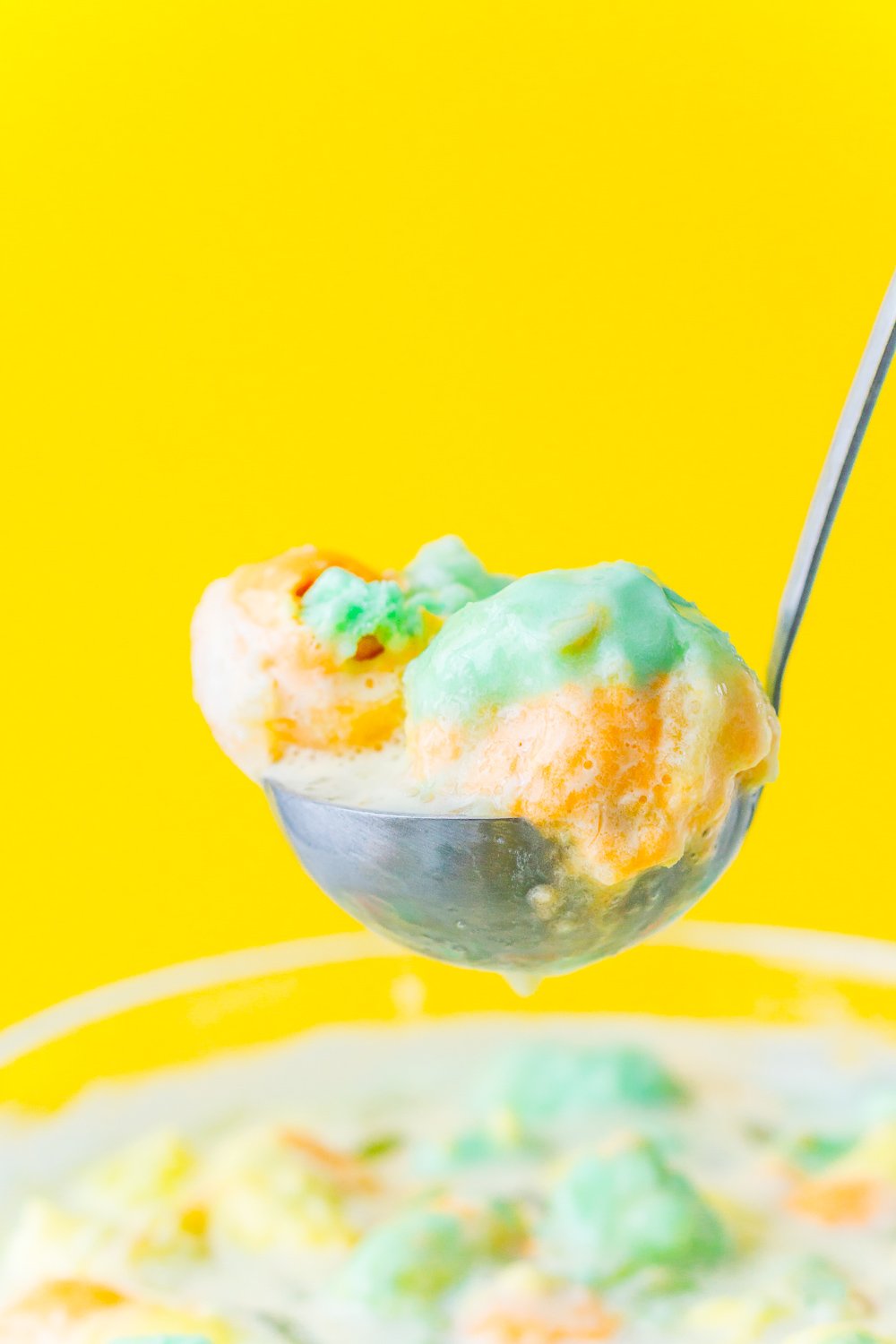 A ladle scooping St. Patrick's Day Punch out of a punch bowl with a yellow background.