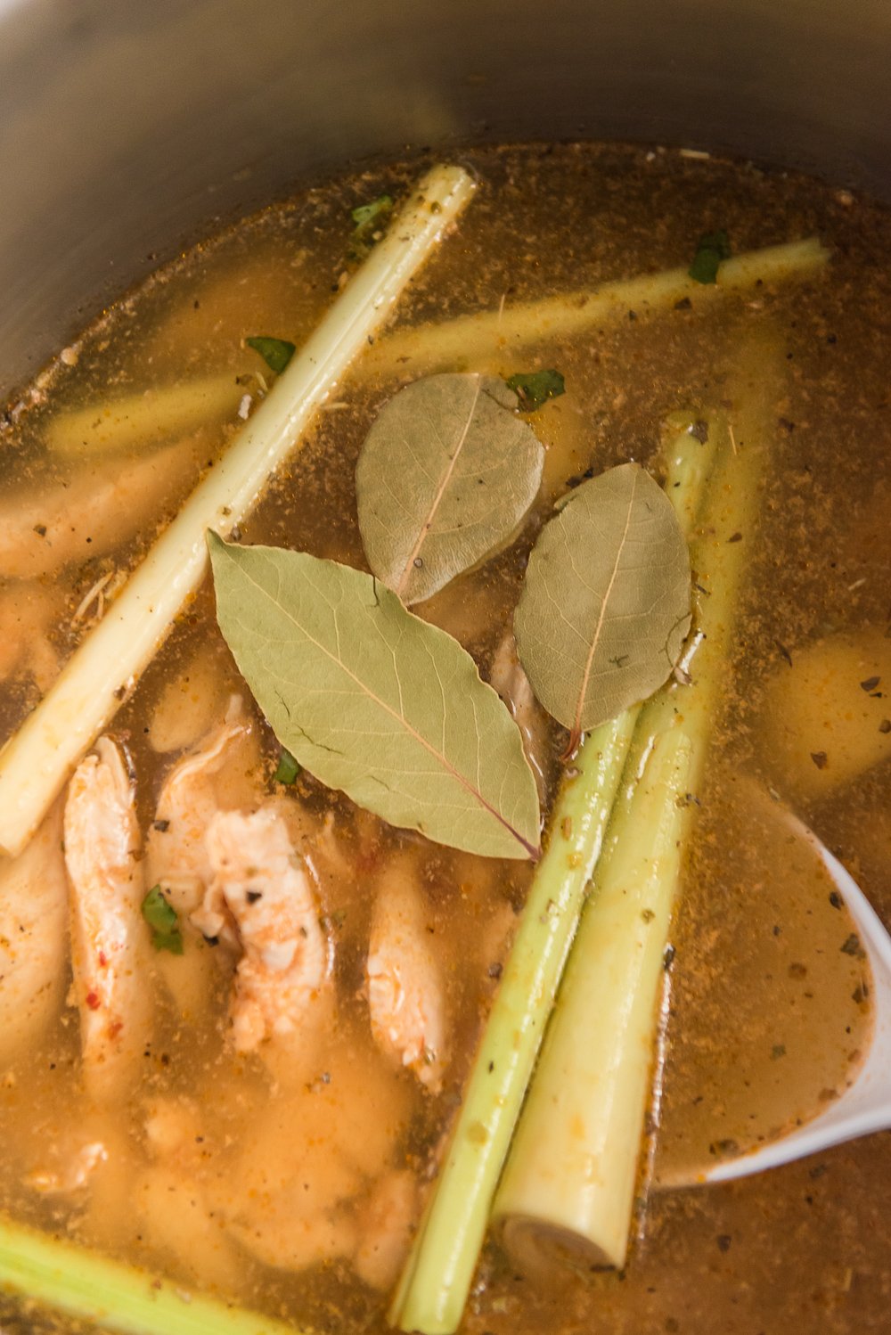 Ingredients for Chicken Coconut Soup (Tom Kha Gai) with broth in saucepan.