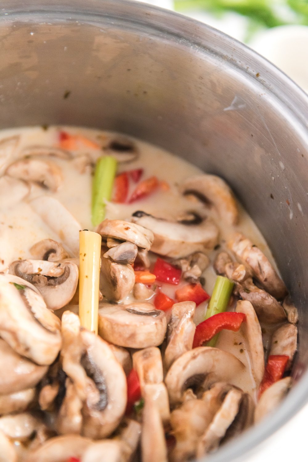 Close up of mushrooms, peppers, and lemongrass in large pot to make chicken coconut soup.