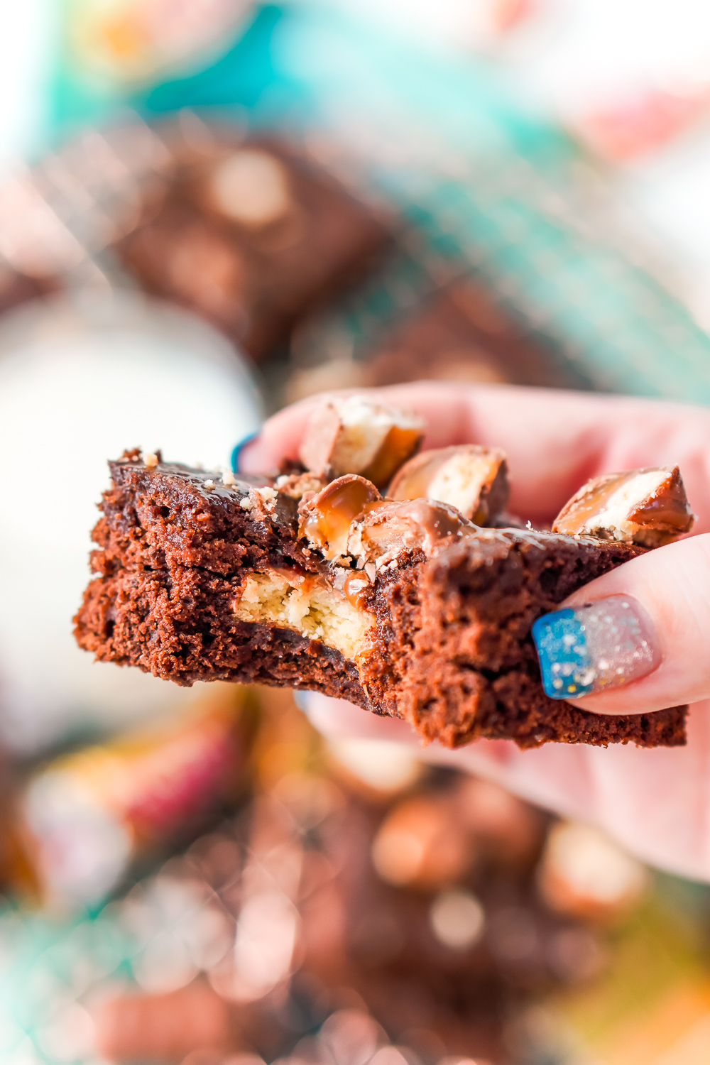 Woman's hand holding a Twix Caramel Brownie with a bite taken out of it.