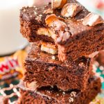 Close up photo of a stack of three Twix Caramel Brownies with a bite taken out of the top brownie.