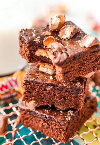 Close up photo of a stack of three Twix Caramel Brownies with a bite taken out of the top brownie.