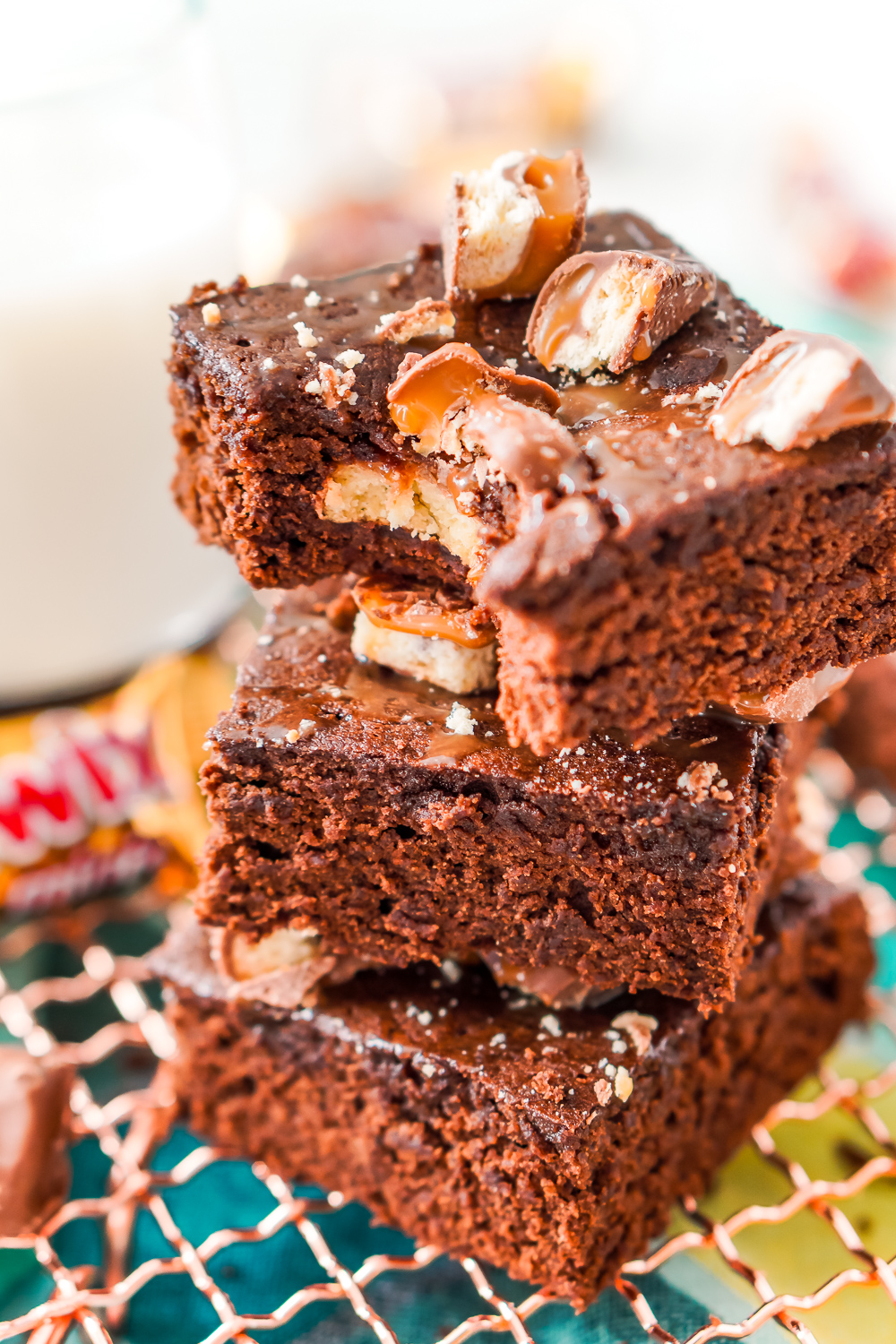 Close up photo of a stack of three Twix Caramel Brownies with a bite taken out of the top brownie.