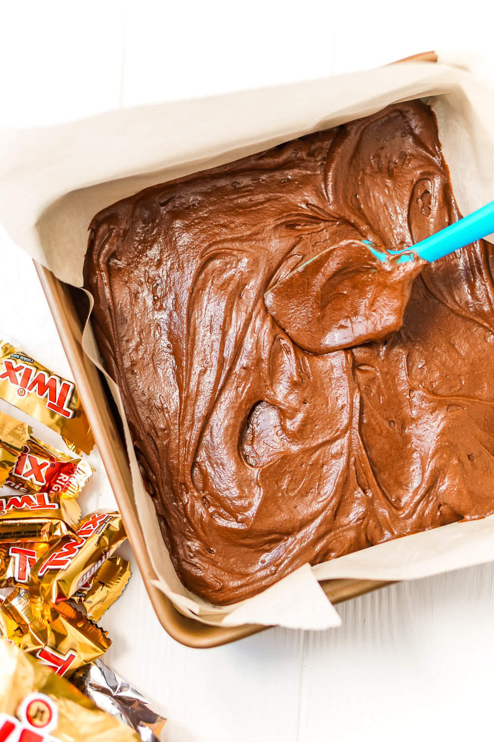 Brownie batter being spread in a baking dish with a rubber spatula.