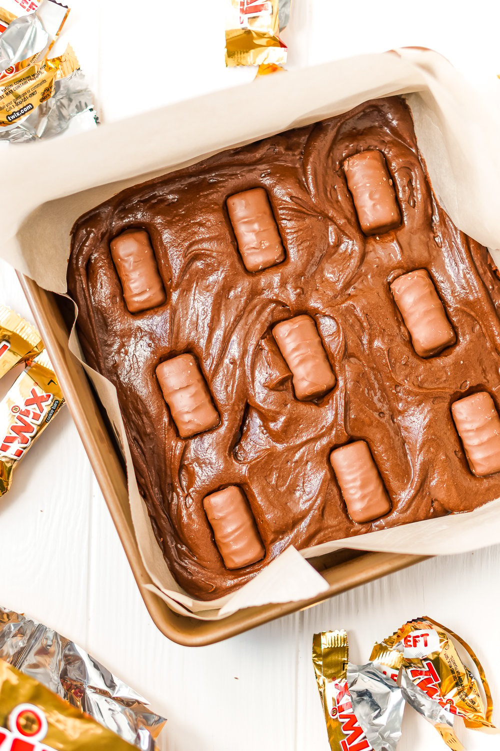 Unbaked brownie batter in baking dish with Twix bars pressed into the batter.
