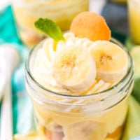 Small jar filled with banana pudding with banana slices, mint leaf, and nilla wafer on top.