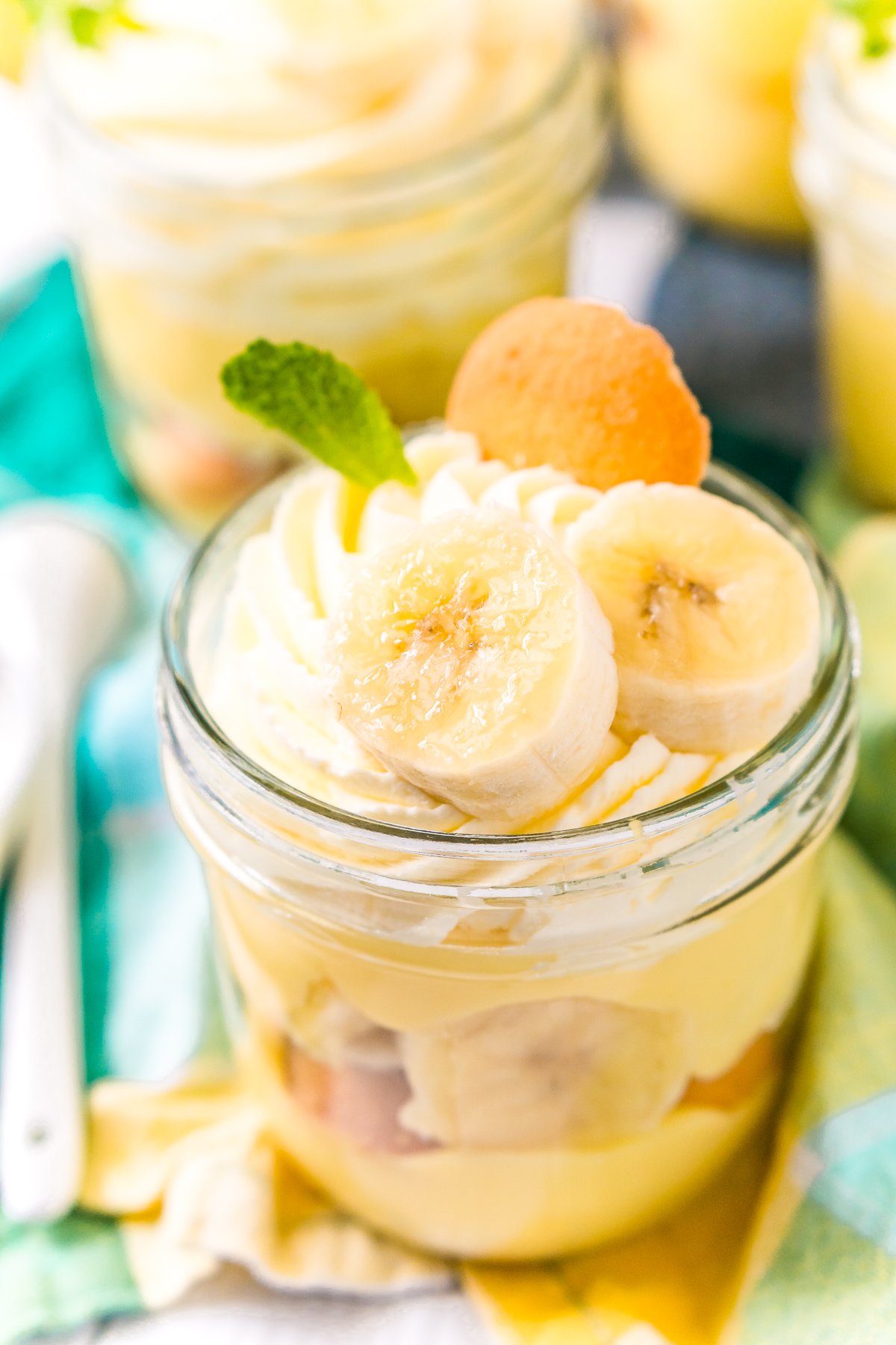 Small jar filled with banana pudding with banana slices, mint leaf, and nilla wafer on top.