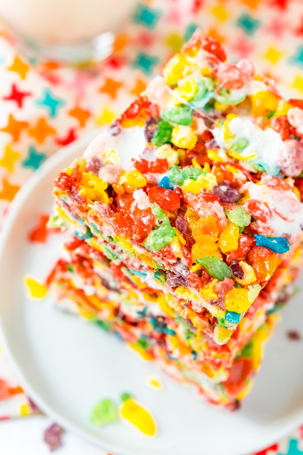 Stack of Fruity Pebbles Treats on a small white plate on a colorful napkin.