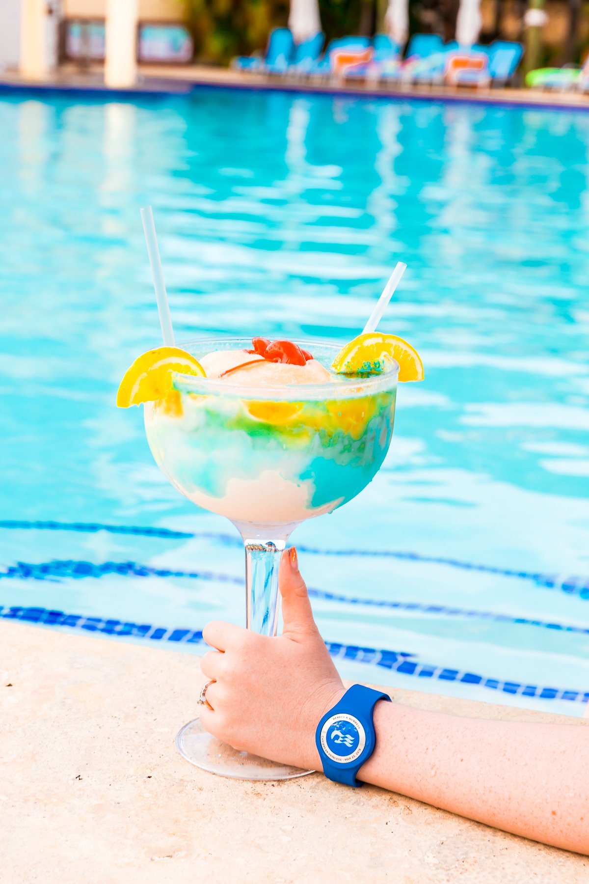 Frozen blue, yellow, and white colada being held by a woman's hand next to a pool.