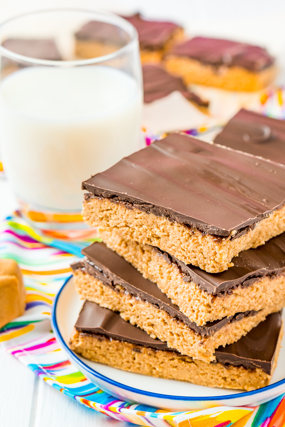 Chocolate Peanut Butter Bars on white plate with blue trim on a coloful napkin next to a glass of milk.