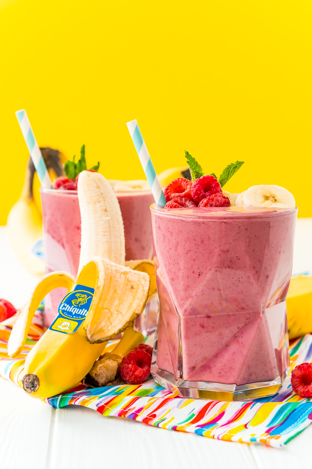 Straight on photo of two glasses filled with raspberry banana smoothie with a banana leaning next to the glass.