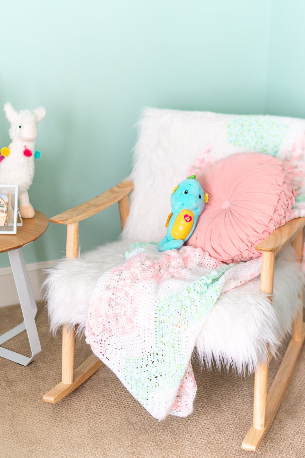 Faux Sheepskin and wooden rocking chair in a baby nursery with a knitted blanket and pink pillow on it.