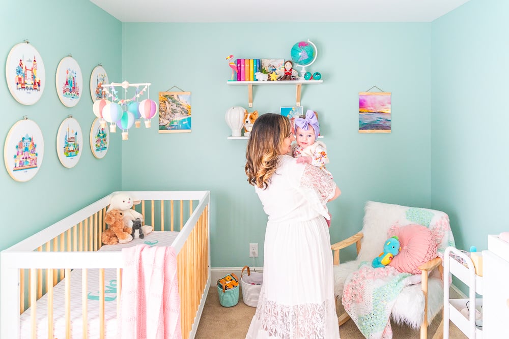 Woman in a white dress with dark hair holding a baby in a travel inspired nursery