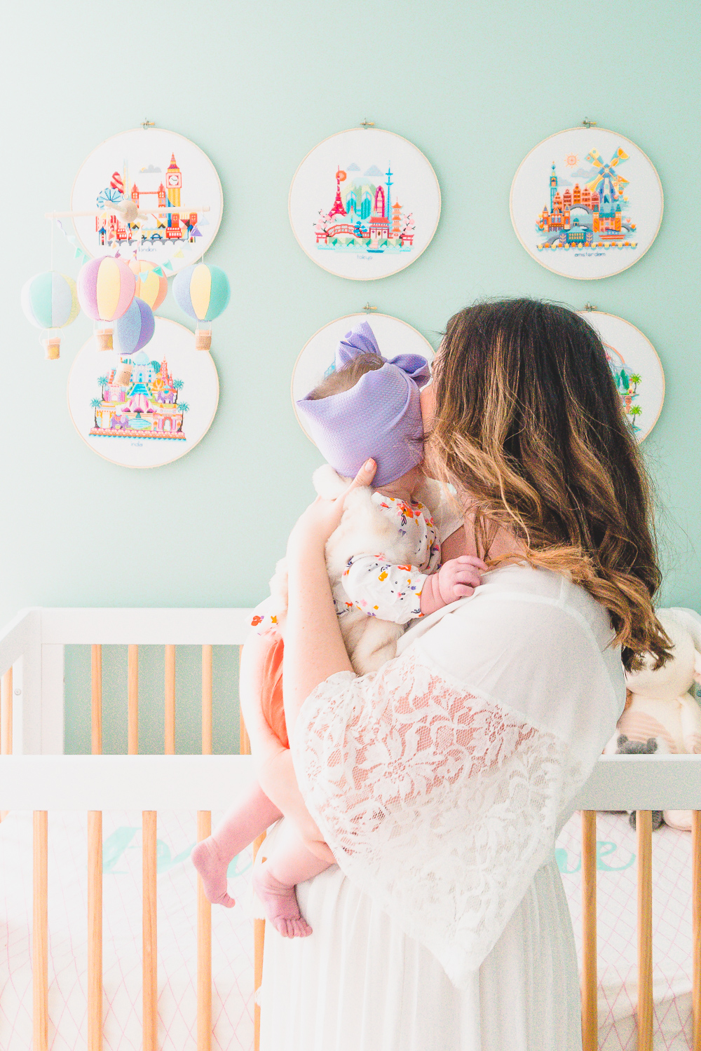 Woman in white dress holding baby girl in front of a crib