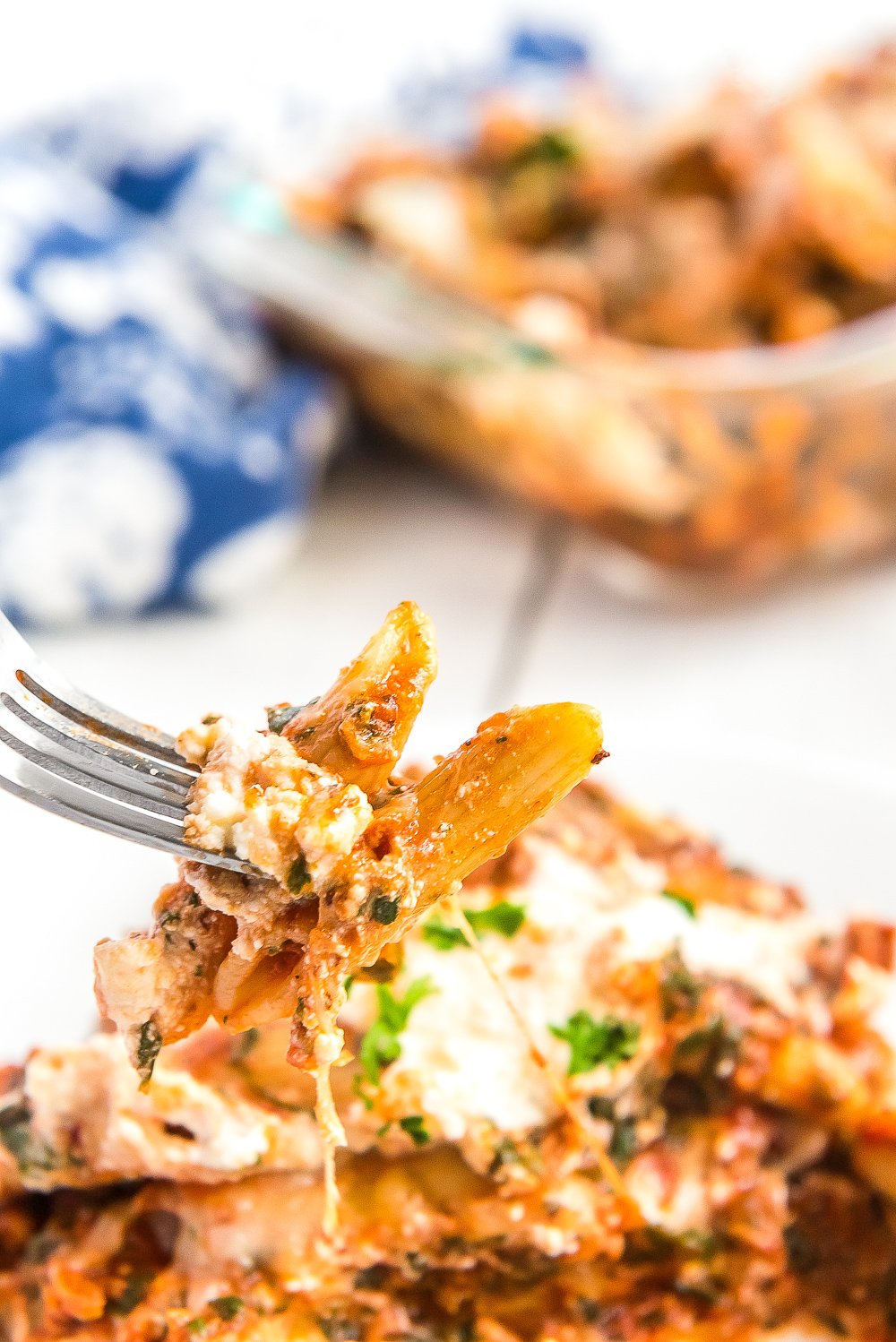 Fork with a bite of penne pasta from a pasta bake on it.