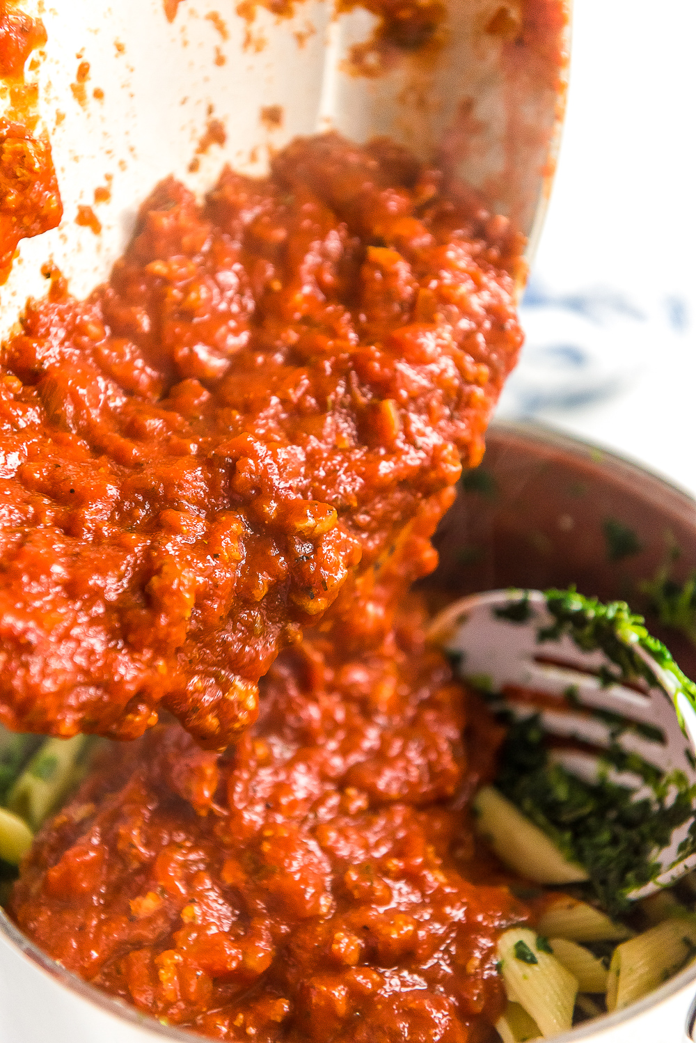 Meat sauce being poured into a pot with pasta and spinach.