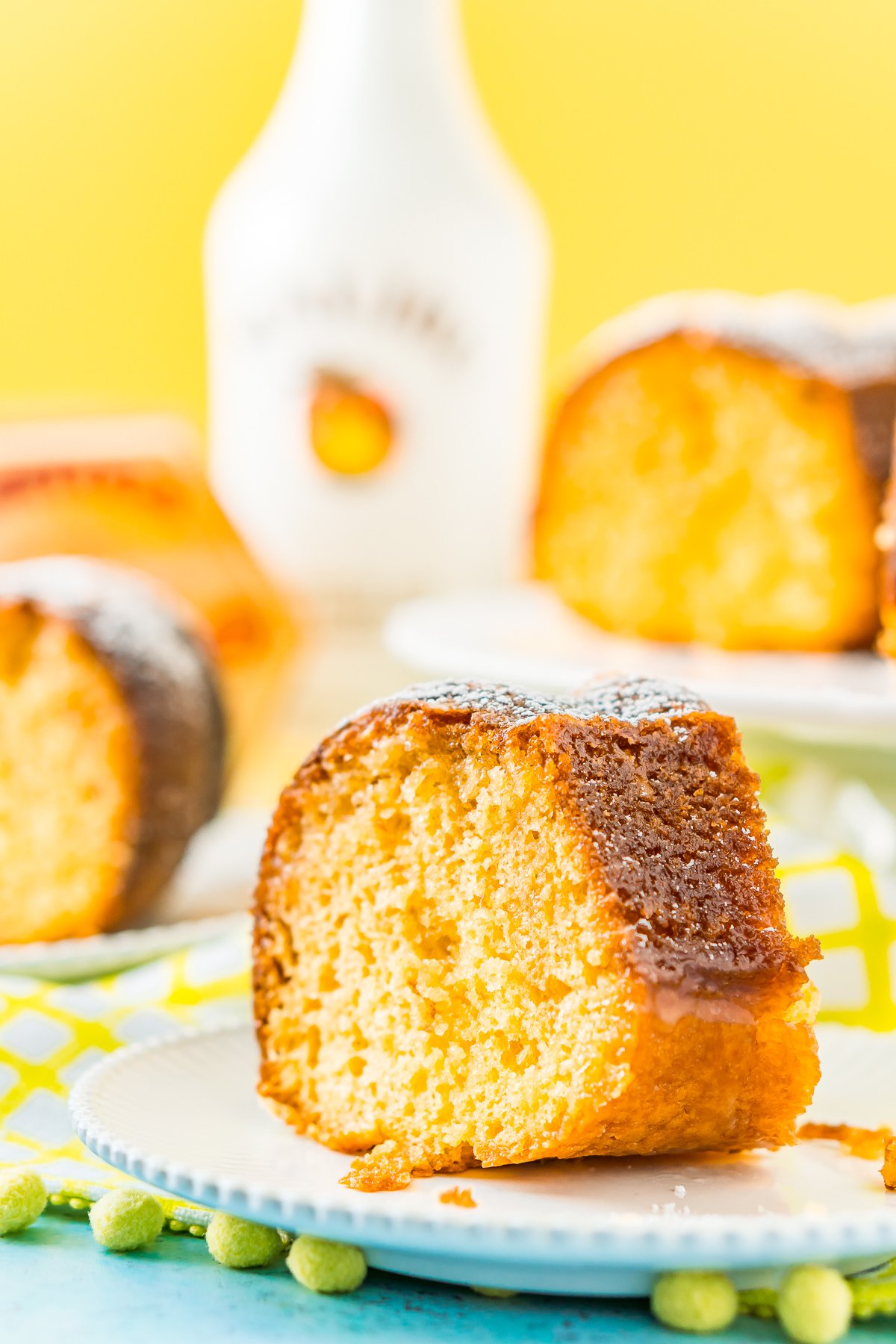 Slices of coconut rum cake on white plates with a bottle of Malibu coconut rum in the background.