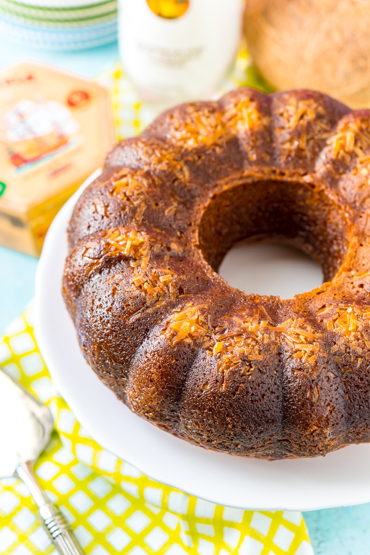 Whole bundt cake with coconut baked into the top on a white cake stand with a bottle of rum in the background.