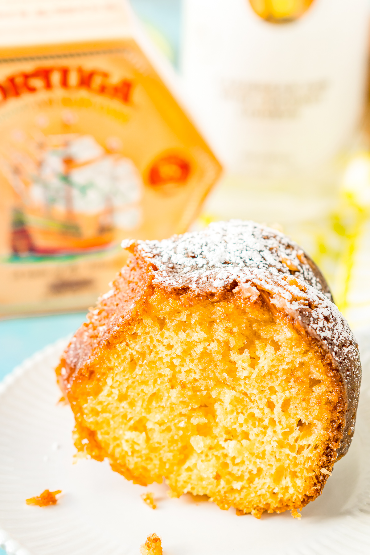 Slice of Coconut Rum Cake sitting on a white plate with a bottle or rum in the background.