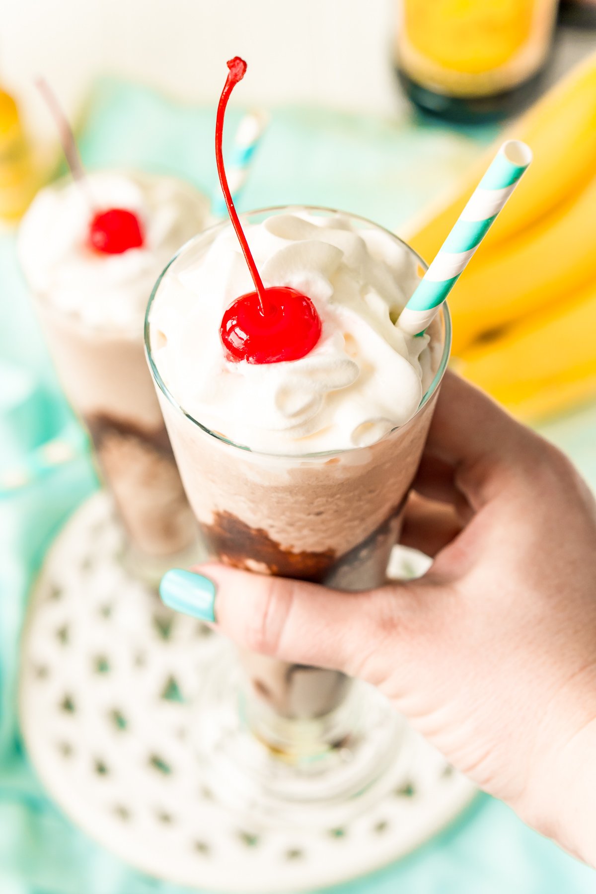 Woman's hand holding a frozen cocktail with whipped cream and a cherry on top.