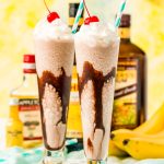 Frozen dirty banana drink in two glasses with bottles of rum and bananas in the background.