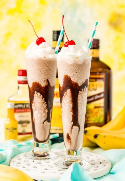 Frozen dirty banana drink in two glasses with bottles of rum and bananas in the background.