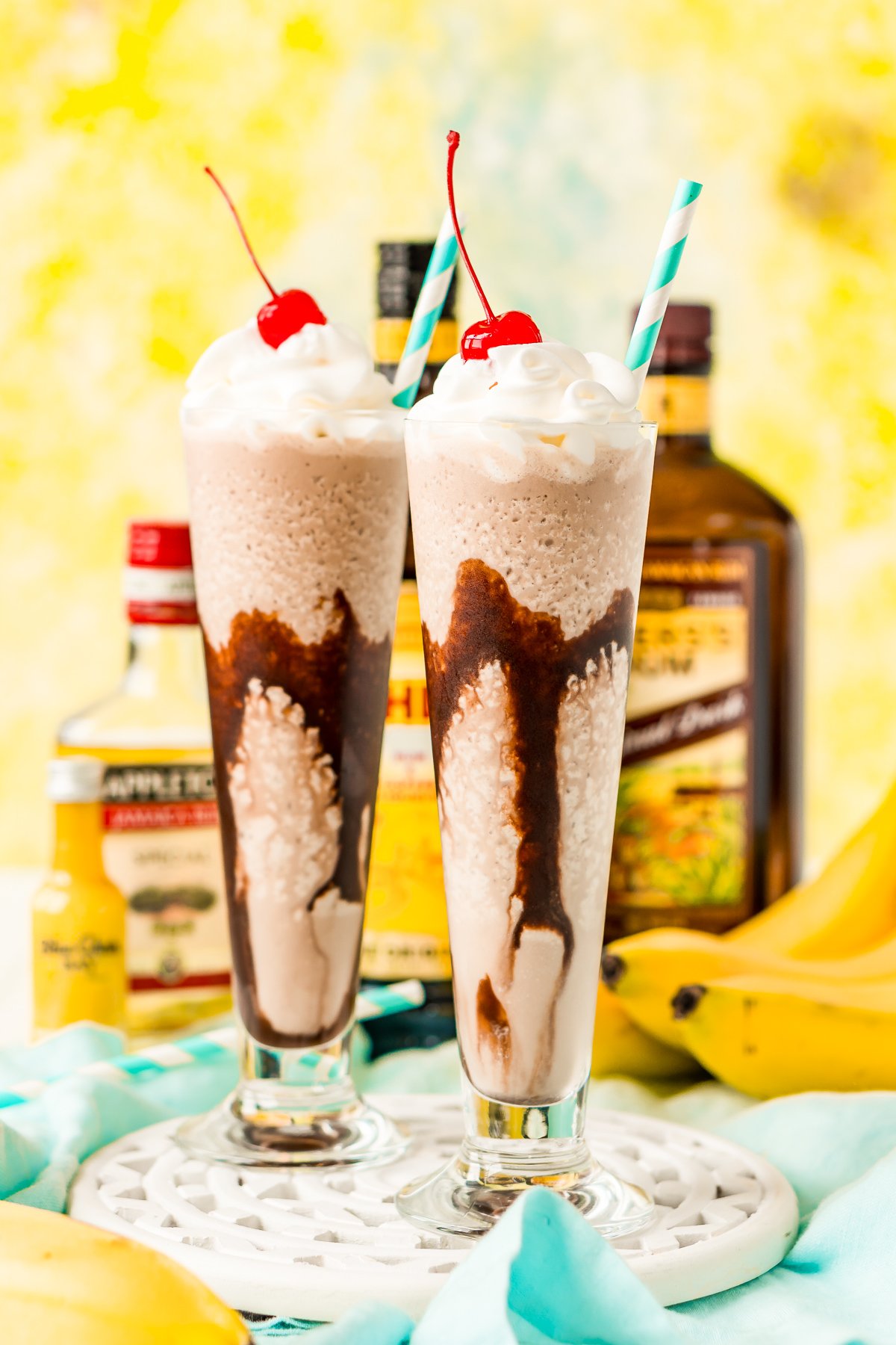 Frozen dirty banana drink in two glasses with bottles of rum and bananas in the background.