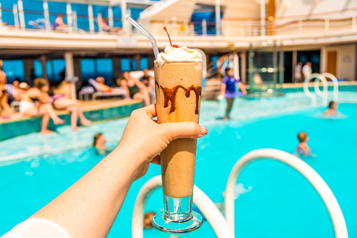 Woman's hand holding a frozen beverage by the pool on a cruise ship.