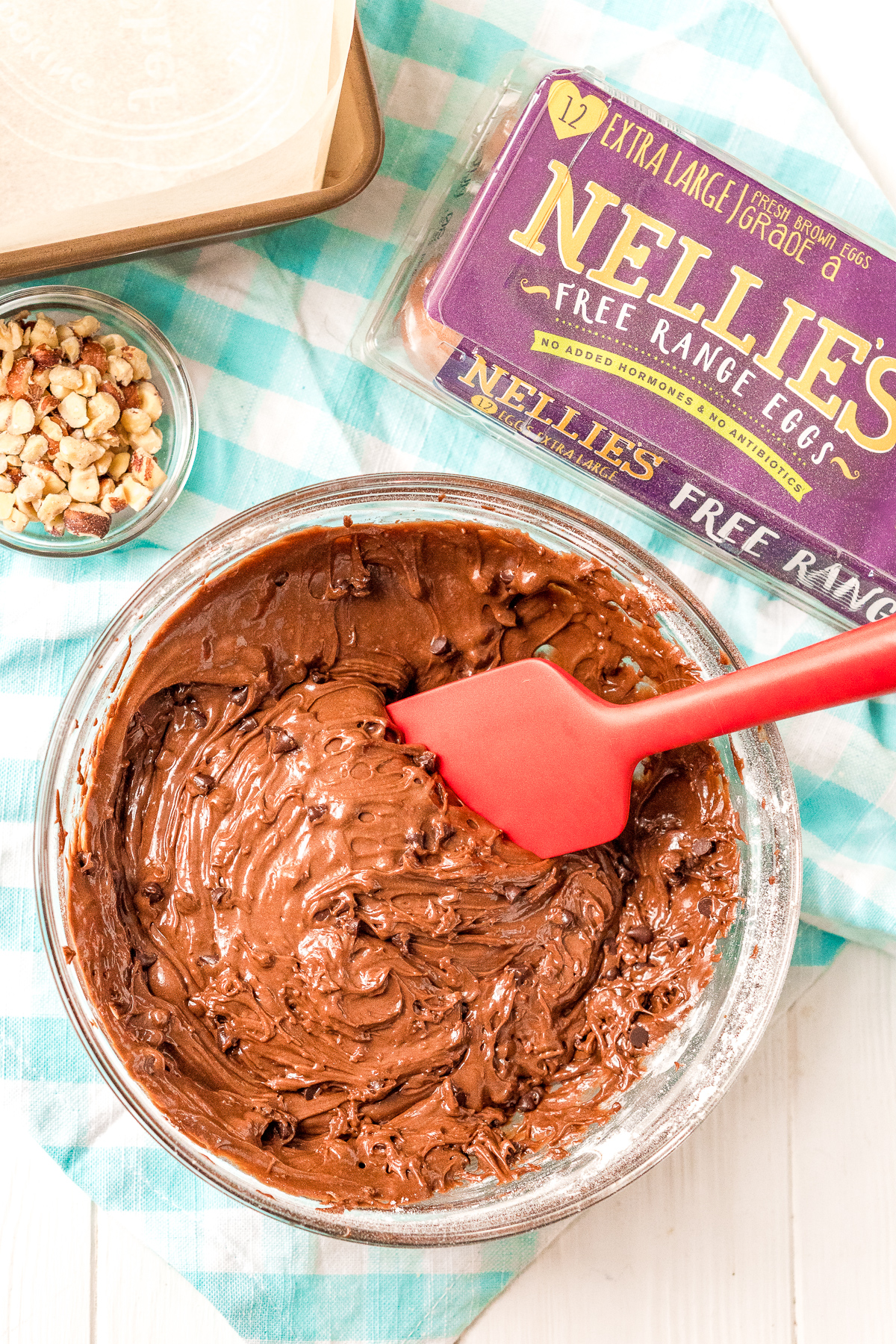 Brownie batter in a large mixing bowl with a smaller bowl of chopped hazelnuts next to it.