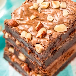 Overhead angled photo of a stack of hazelnut brownies with hazelnuts on top on a blue and white napkin.