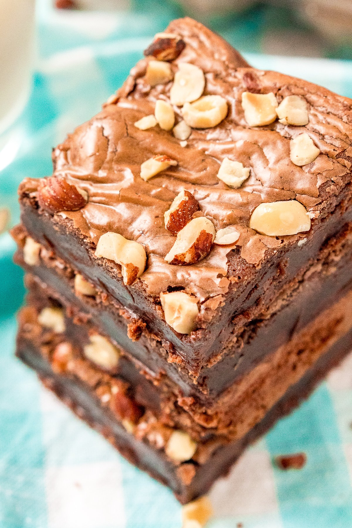 Overhead angled photo of a stack of hazelnut brownies with hazelnuts on top on a blue and white napkin.