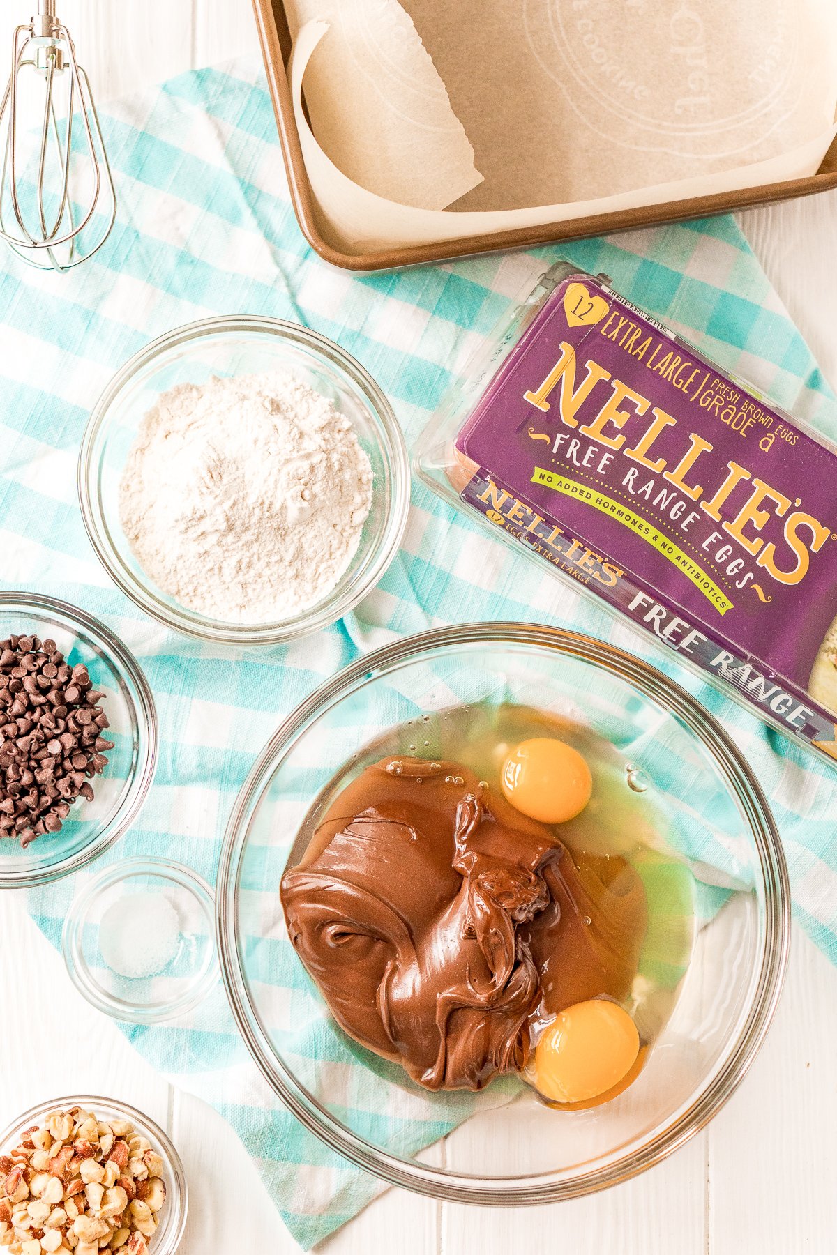 Hazelnut spread in a large bowl with two cracked eggs. Other ingredients in prep bowls scattered around.