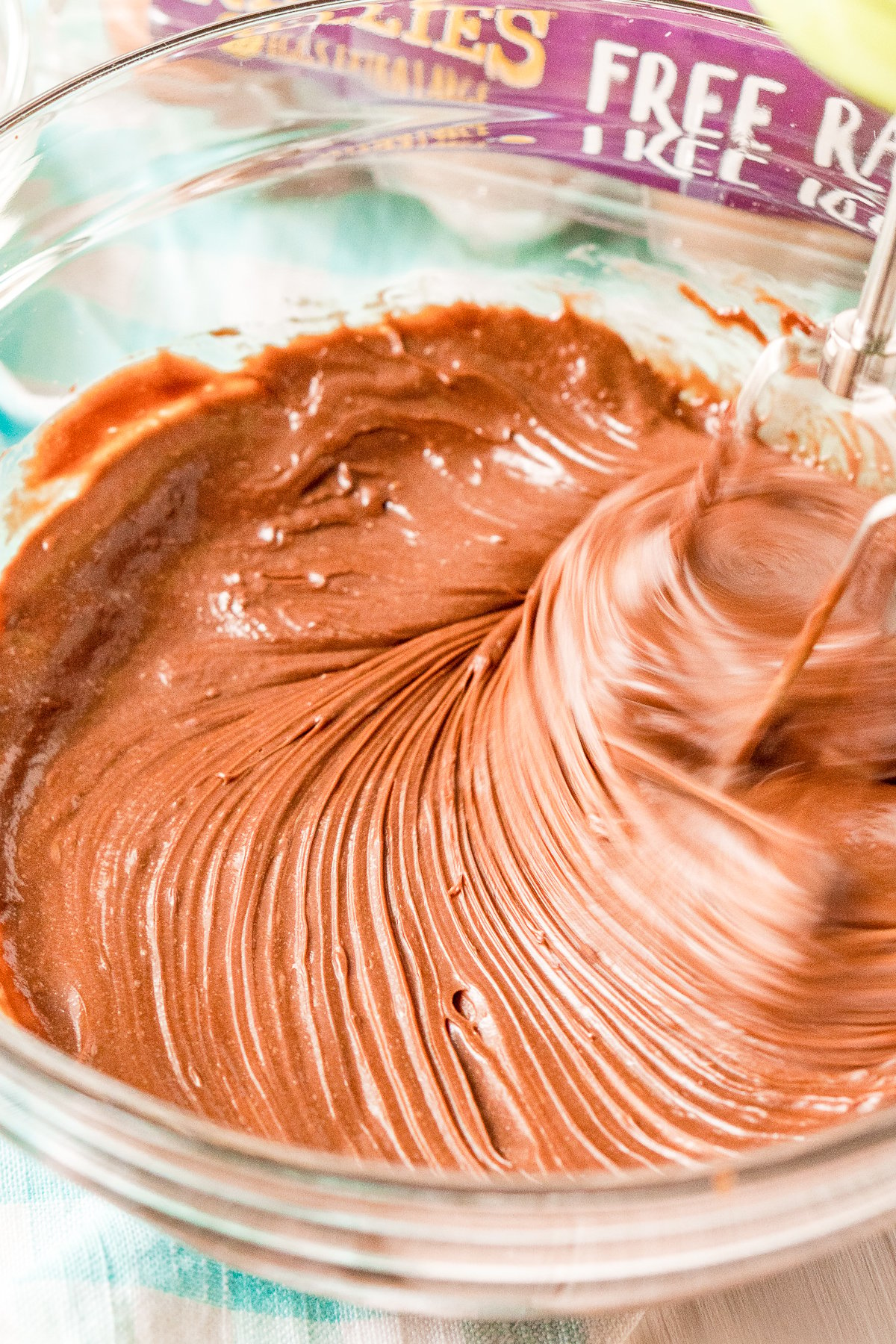 Hand-mixer beating hazelnut spread and eggs together in a large glass bowl.