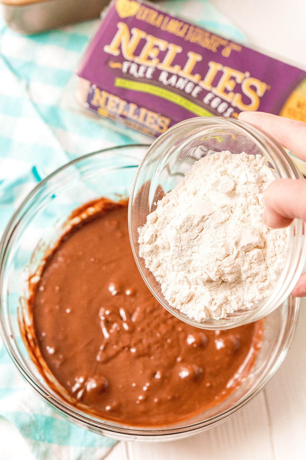 Flour being adding to a bowl of brownie batter.