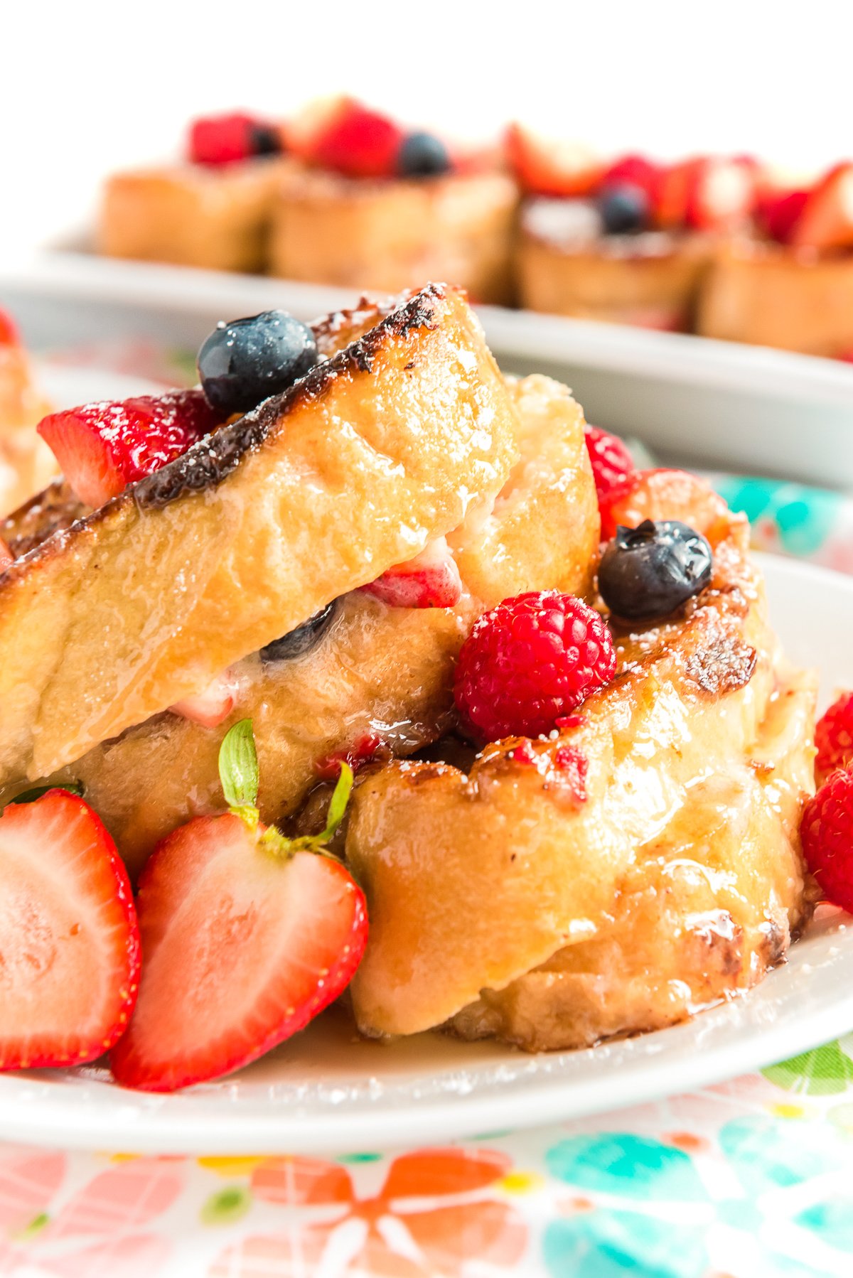 Berry French Toast on a white plate with more slices of french toast on a plate in the background.