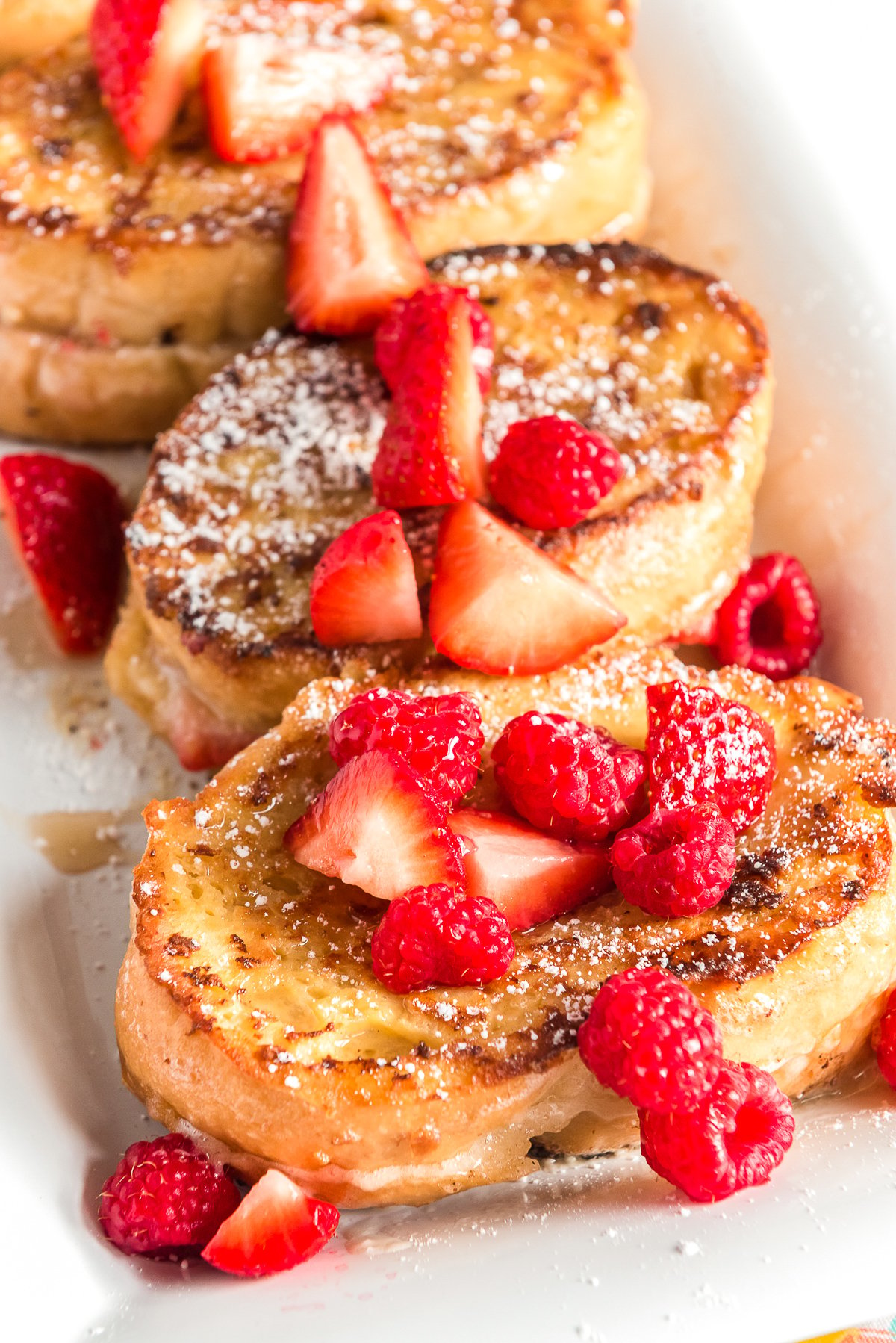 Slices of french toast on a white plate topped with raspberries and strawberries.